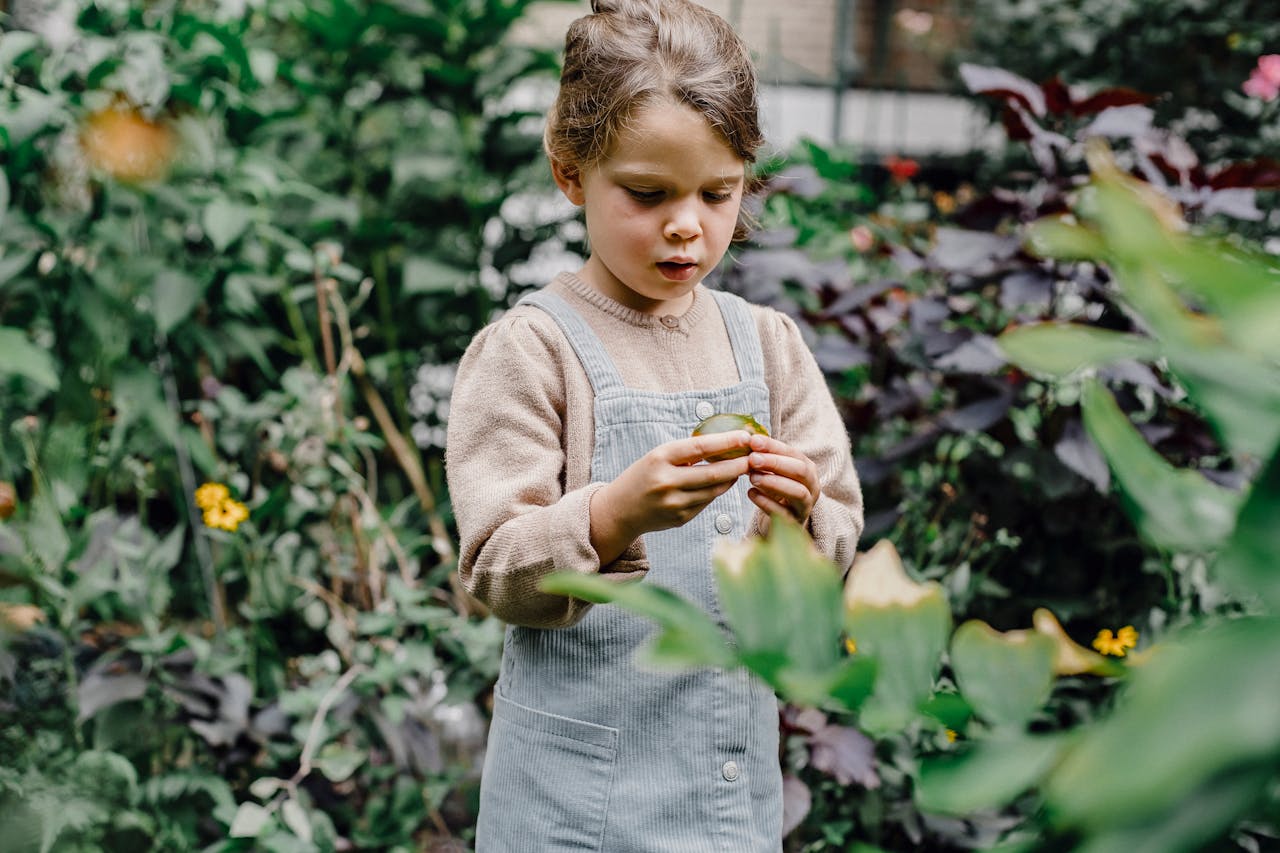 A young girl enjoys exploring fresh foliage in a lush garden setting, highlighting the beauty of nature.